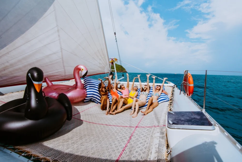 Friends posing on Smile Rainbow Catamaran front net with striped cushions