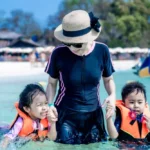 Parent carrying two children through the shallow water at Khai Island