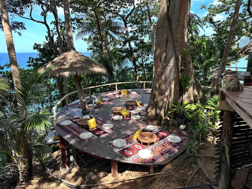 Drinks and food on a shaded wooden platform at A Blanket & A Pillow with the sea beyond