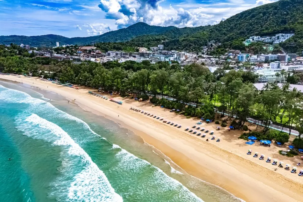 Aerial view of waves reaching the sandy shore and beach umbrellas at Kata Beach