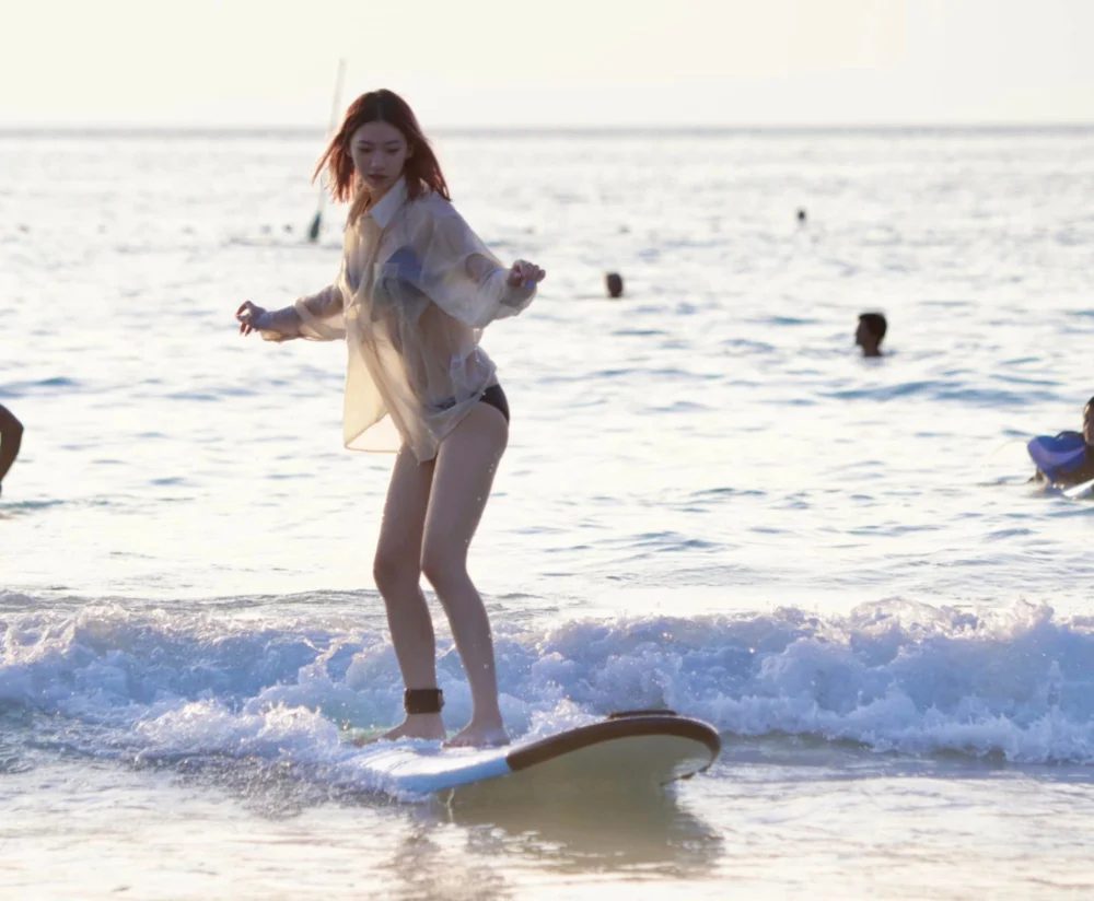 A woman standing on a surfboard in shallow breaking waves at Kata Beach